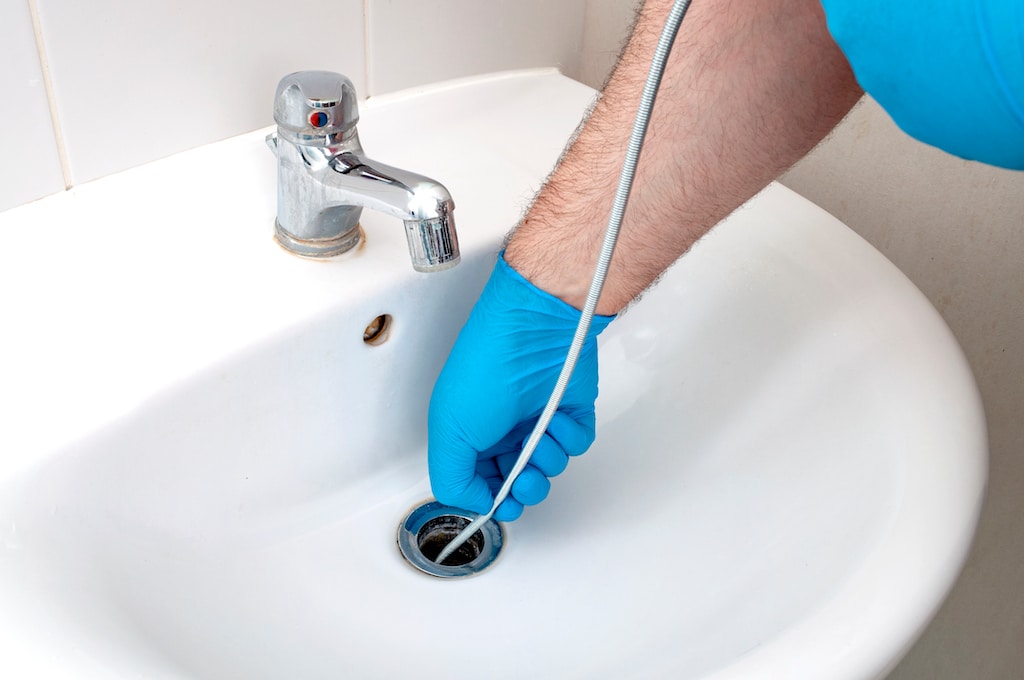 plumber using snake tool to clear drain 