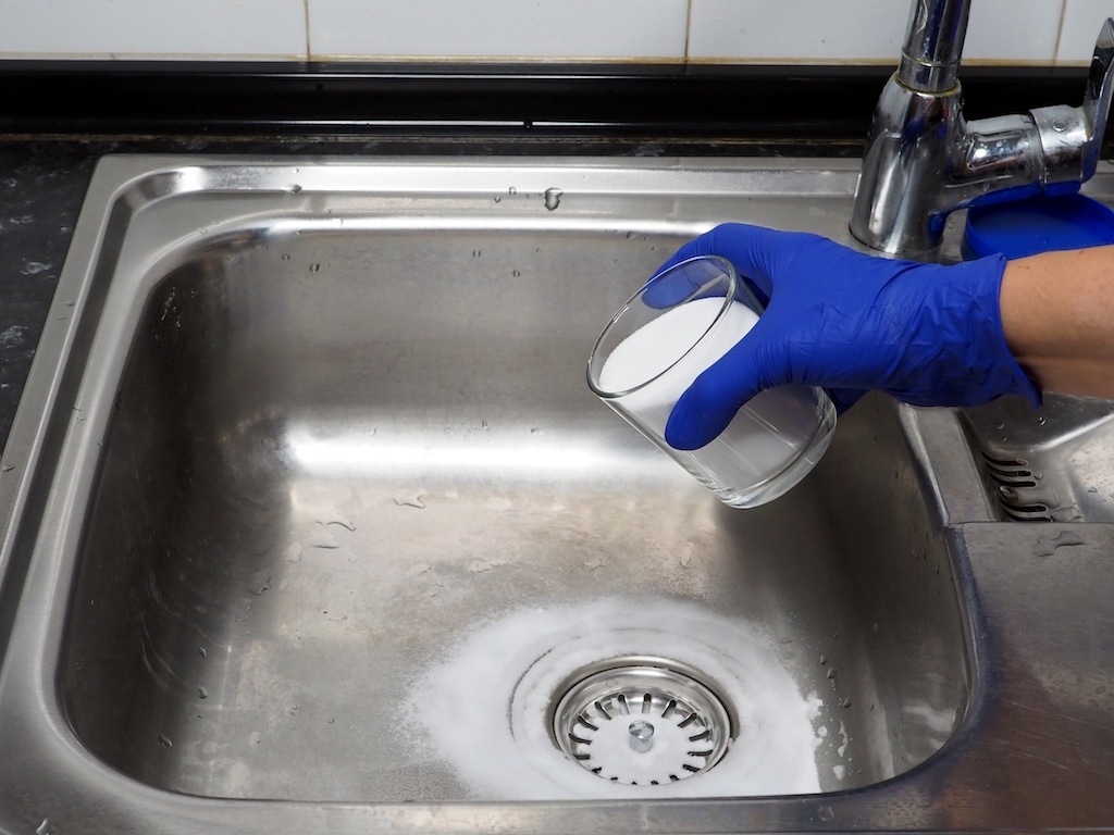 Hand putting baking soda in drain to clear drain clog